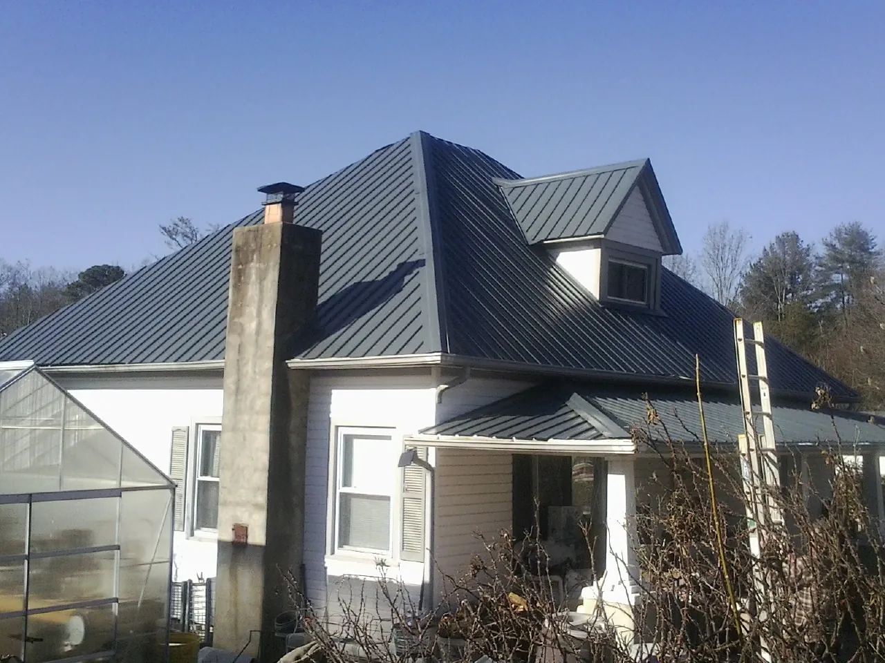 Dark blue standing seam metal roof on a white farmhouse with dormer — Slate & Tile Roof Repair by Roofing Brothers in Comer