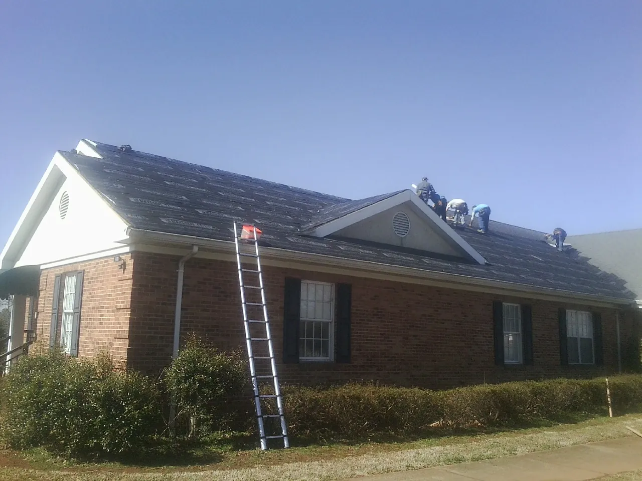 Crew tearing shingles off a brick ranch roof with a ladder set — Emergency Roof Repair work by our crew in Comer