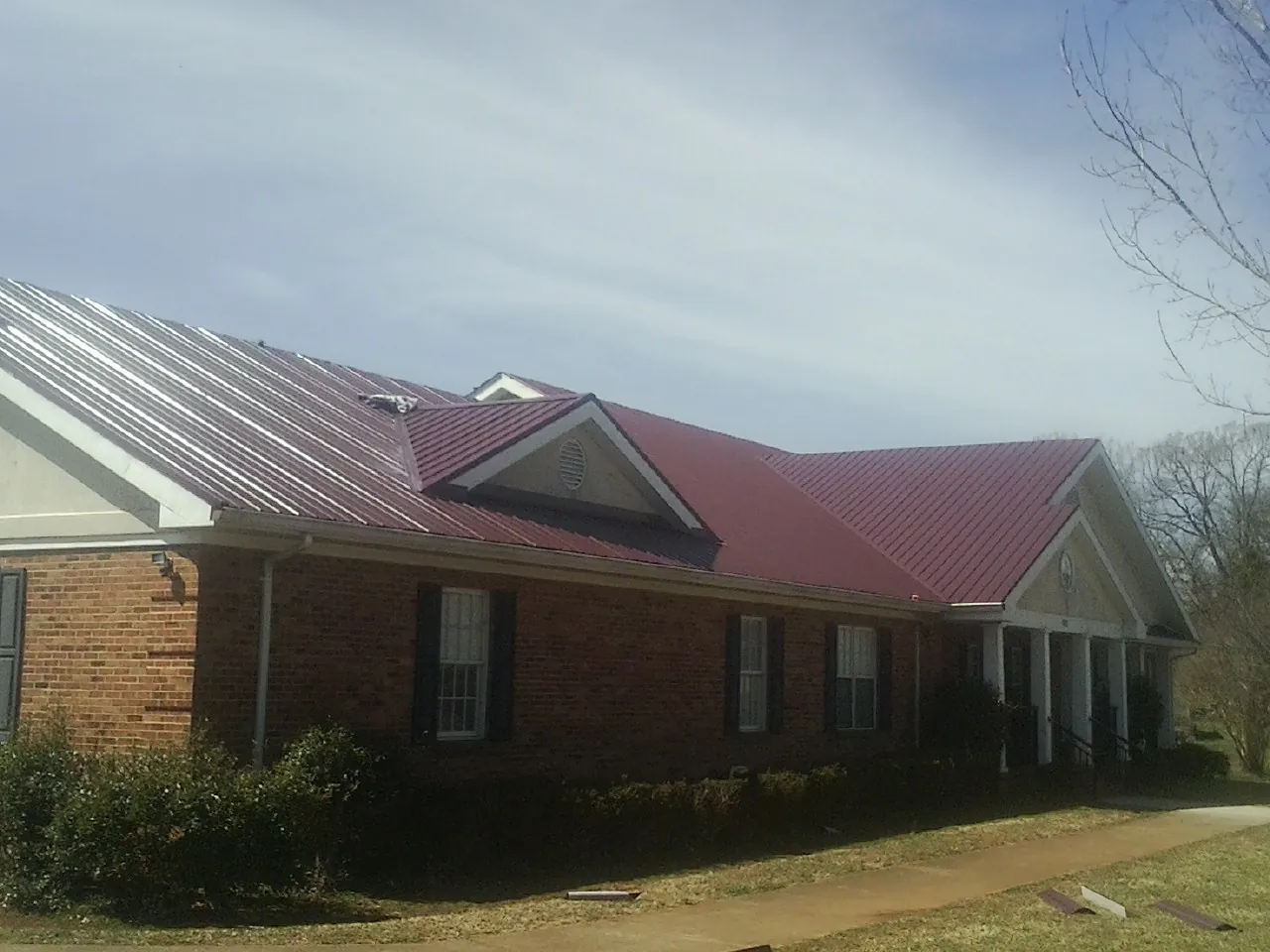 Red metal roof with gabled entries on a long brick building, from a Hail Damage Roof Repair job in Comer