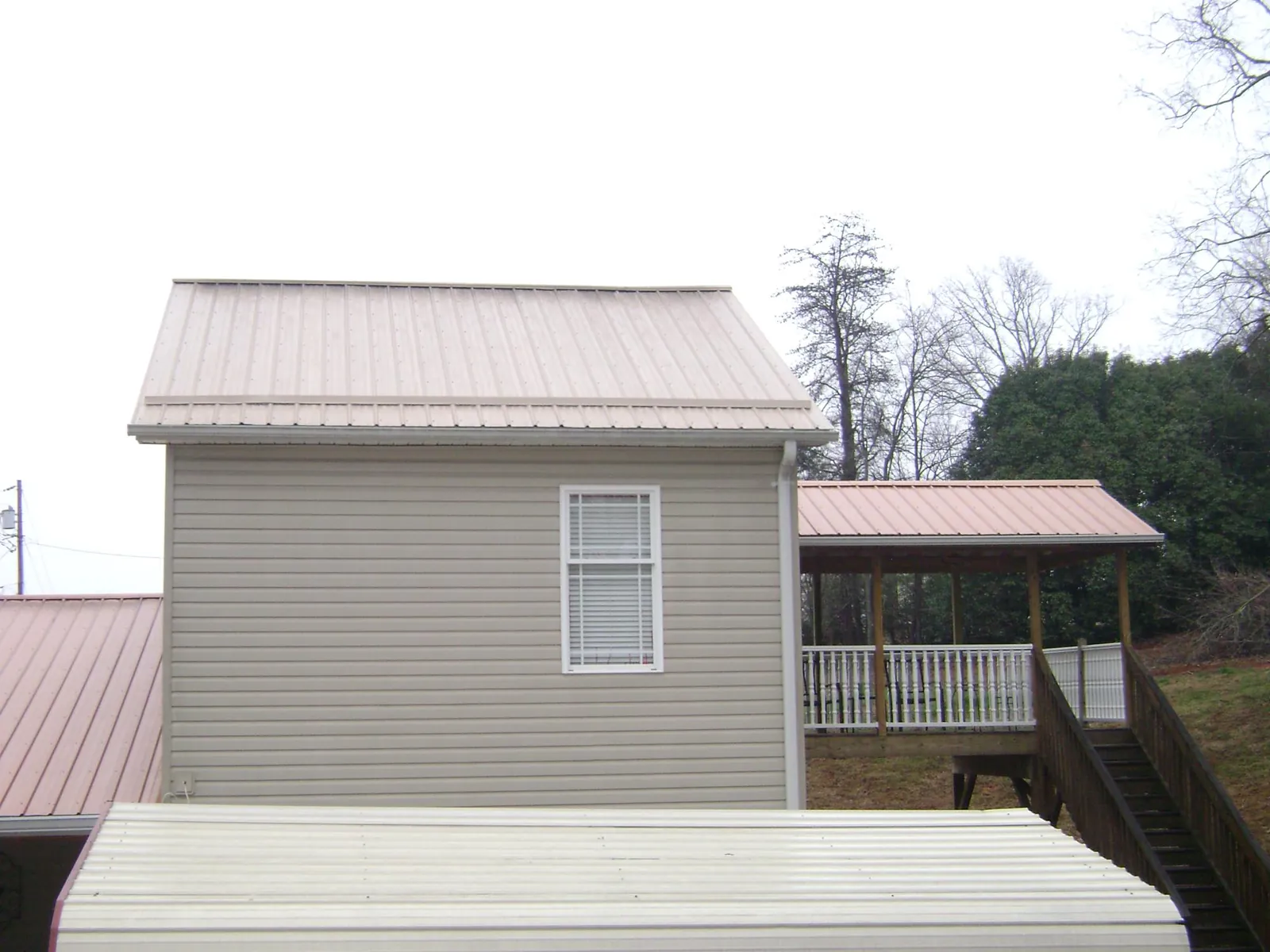 Tan metal roofs on a two story addition and attached porch, from a Roof Replacement job in Comer